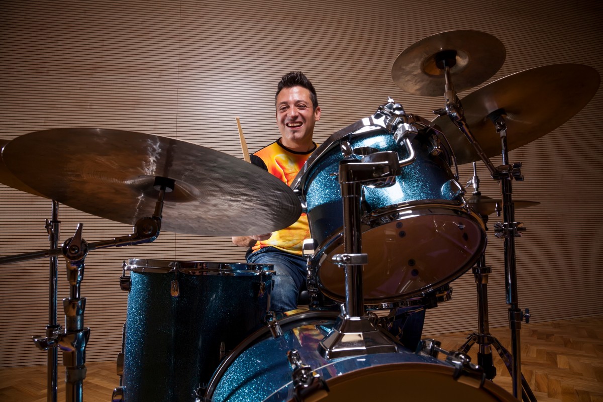 An adult smiling while playing drums